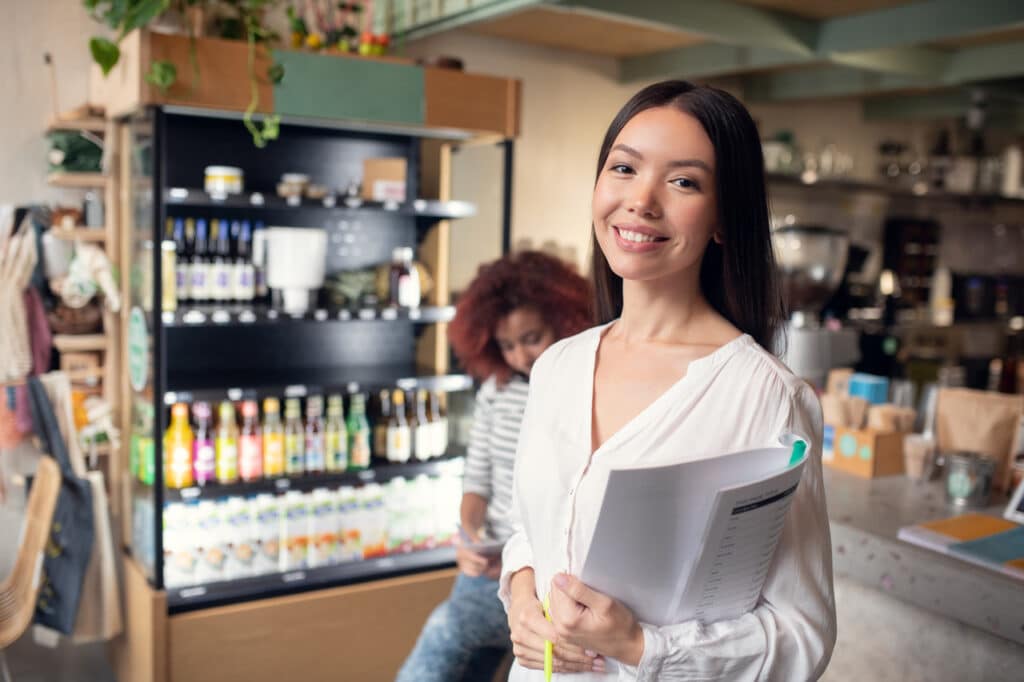 Woman stands in front of a cafe with a few people behind her